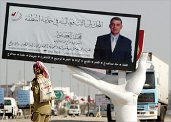 An Arab man walks to a bus stop near a billboard for election candidate Mohammed al Asfoor in the Bahrain town of Budaiya October 23, 2002. Bahrain holds its first parliamentary elections in nearly three decades on October 24, overshadowed by an opposition boycott and fears of sectarian discord. REUTERS/Chris Helgren