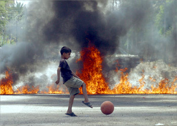 An Iraqi boy plays in front of flames blocking a street in Baghdad's Shiite Sadr City neighborhood 18 May 2004. Residents of Sadr city blocked many roads in Sadr City, in a bid to prevent US military vehicles from entering the poor slums. One Iraqi was killed and five wounded in the holy city of Karbala in night-time clashes between coalition troops and the militia of radical Shiite cleric Moqtada Sadr. AFP PHOTO/Sabah ARAR