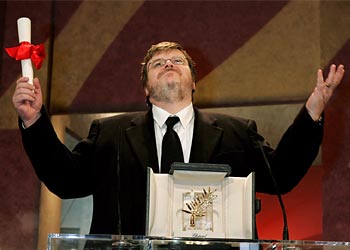 r: U.S. director Michael Moore raises his arms as he reacts to winning the Palme d'Or for his documentary film entry 'Fahrenheit 9/11' as Oscar-winning South African actress Charlize Theron (R)