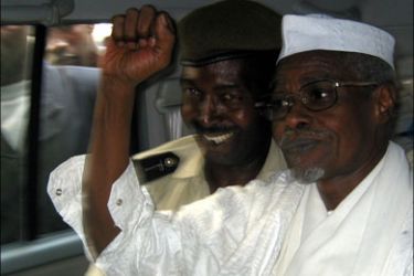 r - Former Chad President Hissene Habre (R) raises his fist in the air as he leaves a court in Dakar escorted by a Senegalese policeman November 25, 2005