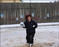 طفل فلسطيني يلهو بالثلج قرب حاجز الرام بالضفة الغربية (الفرنسية)