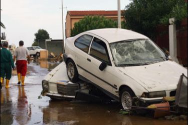 f/People walk past cars piled up in a flooded street of Cagliari, on the italian island of Sardinia on October 23, 2008