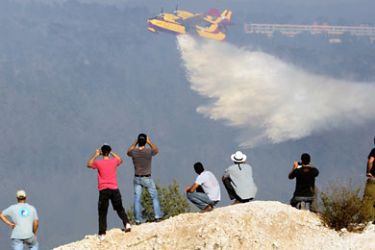 People look on as a firefighter plane drops water during a forest fire over the village of Ein Hod in the Carmel Forest close to Haifa