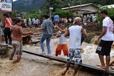 Teres&oacute;polis, Rio de Janeiro, BRAZIL : People cross a flooded street on a makeshift bridge after heavy rains caused mudslides in a low-income neighbourhood in Teresopolis, some 100 km from downtown Rio de Janeiro, Brazil on January 12, 2011. Authorities have stated that more than a thousand people have been left without homes and 230 lost their lives in Teresopolis alone. AFP
