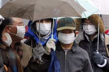 Residents wearing masks and umbrellas line up to buy medicine at a pharmacy during rain and snow in downtown Sendai, northeastern Japan March 16, 2011