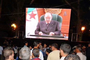 f_People look at Algerian President Abdelaziz Bouteflika delivering a speech on a giant screen, at Amir Abdelkader square in Telemcen on April 15, 2011