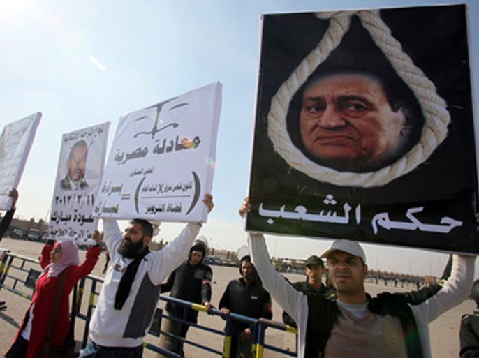 epa03063556 An anti-Mubarak protester (R) holds a placard depicting former president Hosni Mubarak with a hanging rope and words reading in Arabic 'verdict of the people', during Mubarak's trial in Cairo, Egypt, 17 January 2012.