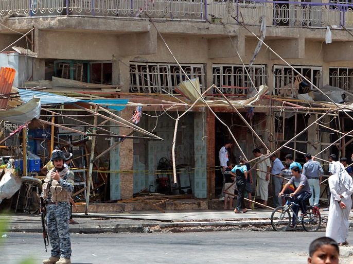 An Iraqi policeman stands guard at the site of a blast as people inspect damages in Baghdad on May 31, 2012. A spate of bombings in Baghdad killed at least 16 people and wounded dozens more, shattering a relative calm with the capital's deadliest violence in weeks. AFP PHOTO/ALI AL-SAADI