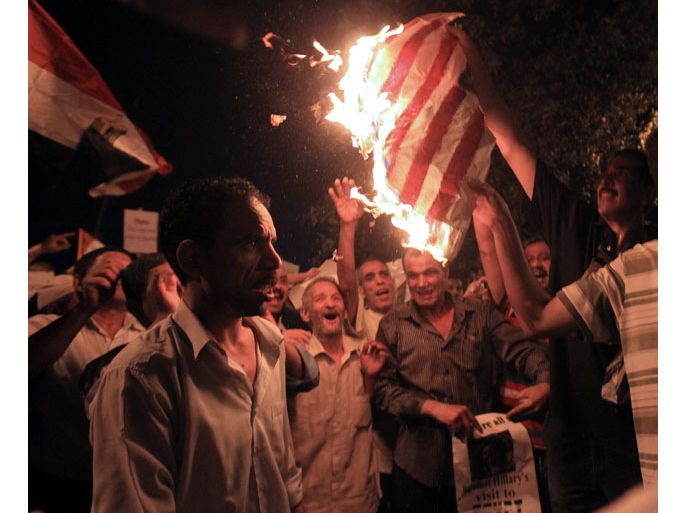 n Egyptian looks on as others burn the US national flag, during a protest against President Mohamed Morsi and the visit of Hillary Clinton to Egypt in Garden City where the US embassy is located, Cairo, Egypt, 14 July 2012. Clinton arrived in Cairo on 14 July and met with President Mohamed Morsi and will also meet with senior government officials, civil society, and business leaders in Cairo, as well as the country's second city Alexandria. Religious freedoms and minority rights are also on her agenda