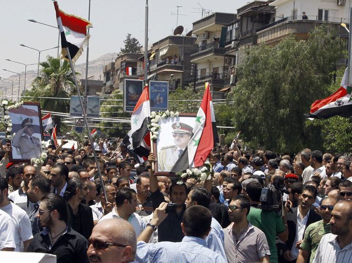 Mourners gather outside the Melkite Catholic Church of the Holy Cross as they wave the Syrian flag and hold images of assassinated Syrian Defense Minister Daoud Rajha during his funeral in Damascus on July 20, 2012. Rajha was killed on July 18, along with two other high ranking Syrian officials by a bomb which
