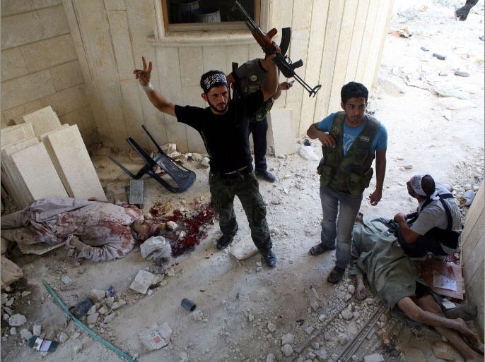 A rebel Free Syrian Army (FSA) fighter flashes the V-sign for victory as he and a comrade stand next the bodies of killed policemen who the FSA allege are “Shabiha” or pro-regime militiamen, on July 31, 2012, as the rebels overran a police station in Aleppo. A watchdog said that rebels killed 40 officers and seized three police stations during the pivotal battle for the commercial capital. AFP PHOTO/EMIN OZMEN/SABAH PRESS