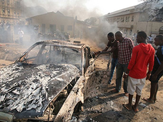 (FILES) Picture taken on December 25, 2011 of men looking at the wreckage of a car following a bomb blast by suspected Nigerian islamist group at St Theresa Catholic Church outside the Nigerian capital Abuja. A ceasefire declaration from a man claiming to represent Nigerian Islamist extremist group Boko Haram spurred intense debate on January 29, 2012 over whether he was a fraud or capable of helping bring peace.