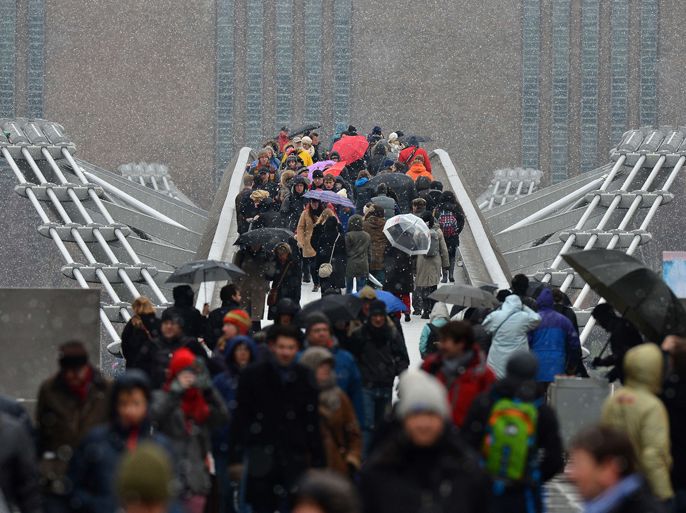 People walk over the Millennium footbridge as snow falls in London on March 23, 2013. Heavy unseasonal snow caused fresh disruption in Britain on March 23, leaving tens of thousands of homes without power, shutting airports and causing an international football match to be called off. AFP