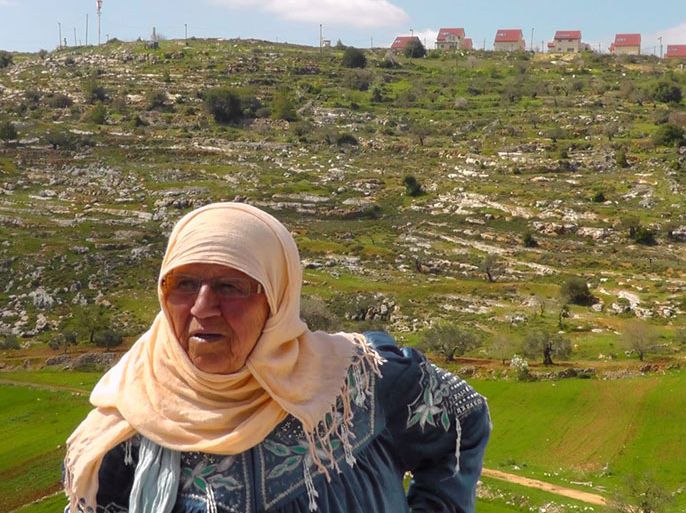 أم فايز البوم تقف على ارضها وقرب منزلها الذي تهدد مستوطنة عيليه بالخلف بمصادرته- الجزيرة نت