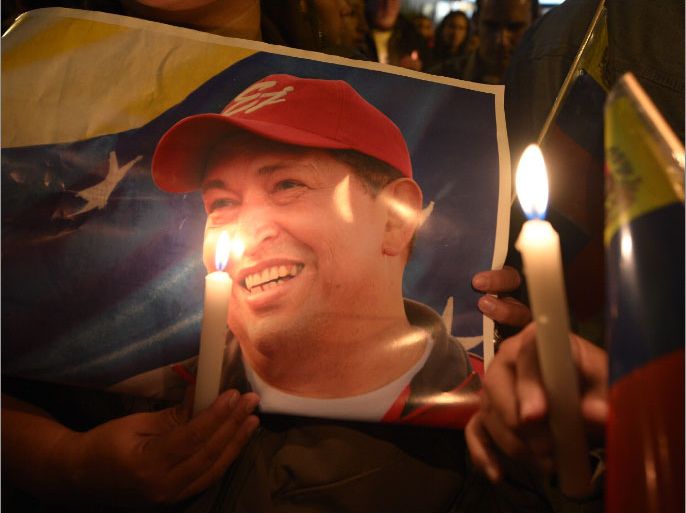 A supporter of Venezuelan President Hugo Chavez holds a poster of him and a candle outside the Venezuelan embassy in Quito on March 5, 2013, after knowing of his death. AFP PHOTO / RODRIGO BUENDIA