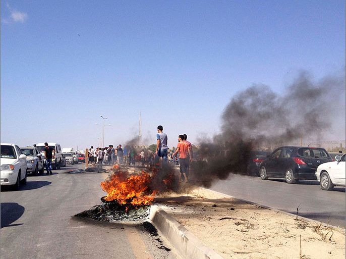 Protesters walk near burning tyres during an attack on a Libyan militia, the Libya Shield brigade, headquarters in Benghazi, June 8, 2013. At least 11 people were killed and 35 wounded in clashes on Saturday between protesters and a Libyan militia operating with Defence Ministry approval in the eastern city of Benghazi, a doctor in the city said. Residents said dozens of protesters had demonstrated outside the headquarters of the Libya Shield brigade demanding the disbanding of militias who have yet to lay down their weapons nearly two years after the overthrow of long-time dictator Muammar Gaddafi. REUTERS/Esam Al-Fetori (LIBYA - Tags: POLITICS CIVIL UNREST)