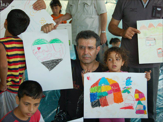 الشاعر نوري الجرّاح يحتضن بعض الأطفال السوريين ورسوماتهم البريئة (الجزيرة)