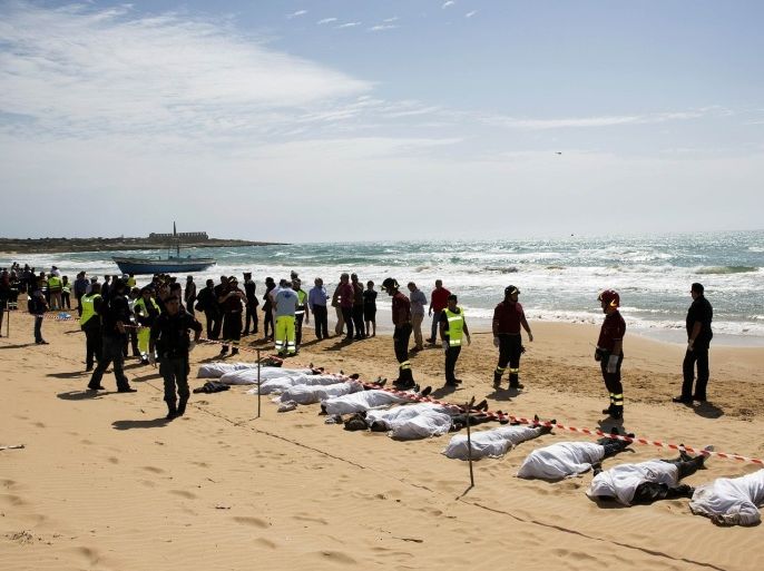 Rescue workers stand next to bodies of migrants who drowned lie on the beach in the Sicilian village of Sampieri September 30, 2013. At least 13 people on a migrant boat arriving in Sicily drowned close to the coast near the eastern city of Ragusa, apparently after trying to disembark from their stranded vessel, Italian authorities said on Monday. Officials said the boat was carrying around 250 people but there was no immediate word on where they came from.