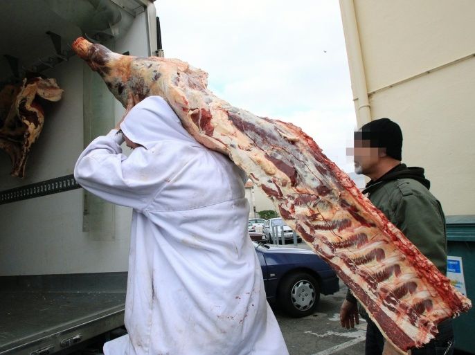 A requisitioned employee (L) carries a piece of meat under the surveillance of a policeman on December 16, 2013, at a butchery's depot in Narbonne, southern France. Twenty-one individuals were arrested on December 16 in southern France as part of an operation against an alleged horse meat traffic. Horses that had been used by pharmaceutical firms could have ended in the food-processing industry. AFP PHOTO / RAYMOND ROIG