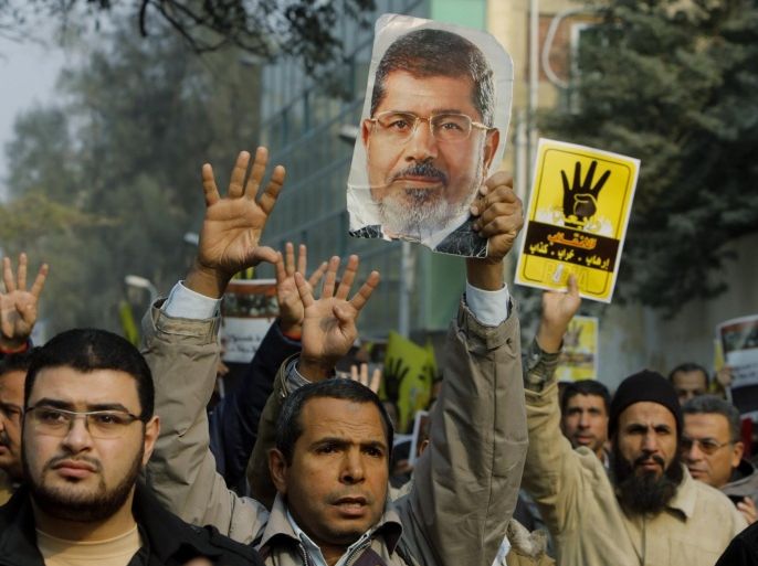 Supporters of Egypt's ousted President Mohammed Morsi hold his poster as they raise their hands with four fingers, which has become a symbol of the Rabaah al-Adawiya mosque, where Morsi supporters had held a sit-in for weeks that was violently dispersed in August, during a protest in Cairo, Egypt, Friday, Dec. 20, 2013. (AP Photo/Amr Nabil)