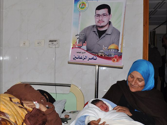 أم تامر الزعانين تحمل حفيدها وإلى جوارها والدة الطفل وأعلاهما صورة للأسير -تقرير: "الحسن" أول طفل لأسير بغزة من نطفة مهربة
