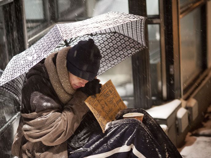epa04006767 A homeless man seeks shelter under an umbrella as he sits begging in front of a store in New York, USA, 03 January 2014. A severe snow storm hit the large area of Northeastern US including the city of New York with an expected dump of 15 inches (38 cm) of snow. The storm is predicted to combine with deep cold and strong winds resulting in blizzard warnings for coastal areas. EPA/SEBASTIAN GABRIEL
