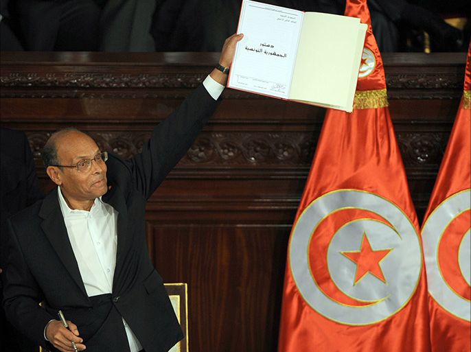 Tunisian president Moncef Marzouki shows a copy of the new constitution after its adoption on January 27, 2014 during a ceremony at the NCA in Tunis. Tunisia's leaders, Marzouki, outgoing premier Ali Larayedh and assembly speaker Mustapha Ben Jaafar, signed the new constitution, a landmark event in the birthplace of the Arab Spring.    AFP PHOTO / FETHI BELAID