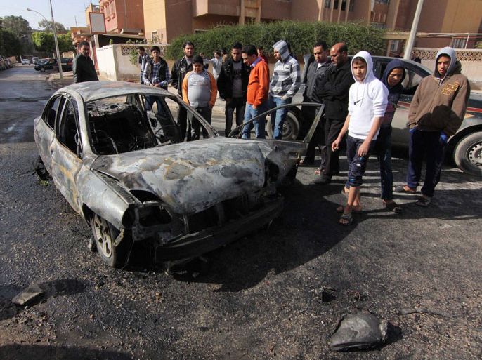 epa04000629 Libyans stand next to the wreckage of a car, belonging to the son of a Libyan navy colonel, that exploded in Benghazi, eastern Libya