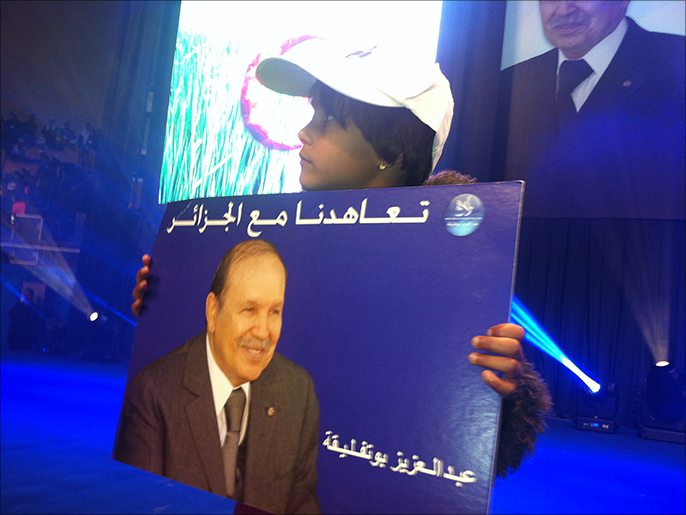 أحد مؤيدي ترشح بوتفليقة يرفع صورته أثناء تجمع في العاصمة الجزائر (الجزيرة)