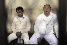 FILE - In this Thursday, Feb. 24, 2011 file photo, former Egyptian Tourism Minister Zuheir Garana, right, and steel tycoon and prominent ruling party leader Ahmed Ezz, left, wearing white prison uniforms, sit in a metal cage as they appear in the Cairo Criminal Court in Cairo, Egypt. An Egyptian court has convicted a Hosni Mubarak-era steel tycoon of profiteering and squandering public funds, and sentenced him to 37 years in prison. The court Wednesday found Ezz guilty of making illicit gains of $740 million in a number of illegal business deals involving his steel firm.
