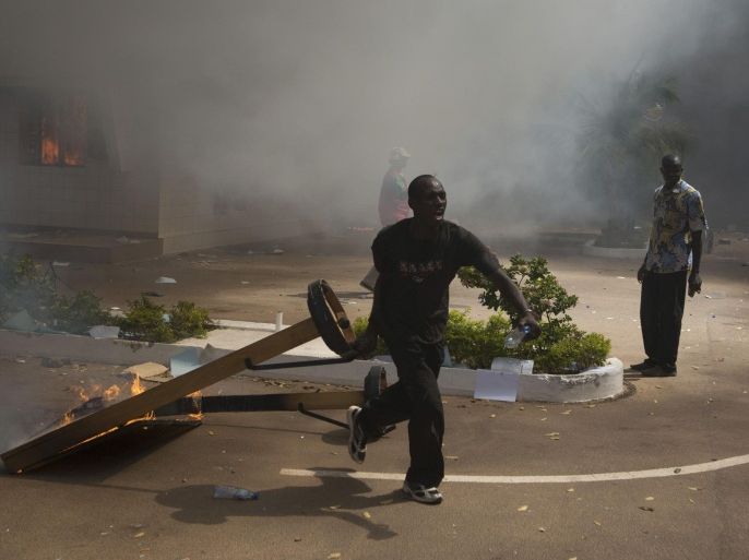 An anti-government protester carries a burning object outside the parliament building in Ouagadougou, capital of Burkina Faso, October 30, 2014. Tens of thousands of protesters demanding the ousting of Burkina Faso's veteran President Blaise Compaore faced off with security forces outside the presidential palace after burning parliament and ransacking state television on Thursday. REUTERS/Joe Penney (BURKINA FASO - Tags: POLITICS VIOLENCE CIVIL UNREST)