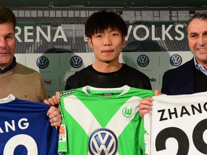 Newly signed Chinese player Zhang Xizhe (C) who will play for German first division Bundesliga football club VfB Wolfsburg, Wolfsburg's sporting director Klaus Allofs (R) and Wolfsburg coach Dieter Hecking (L) display Zhang's jerseys during a press conference in Wolfsburg, central Germany, on December 16, 2014. AFP PHOTO / JOHN MacDOUGALL