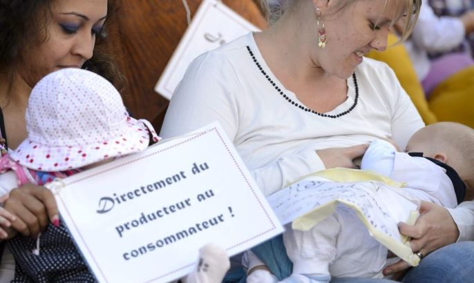 A mother holds a sign reading 'Directly from producer to consumer!' as she nurses a baby during a flashmob protest to promote breastfeeding during the at the Place de la Riponne, in Lausanne, 13 September 2014. Some 50 women gathered and breastfed their baby in public to promote the World Breastfeeding Week 2014.
