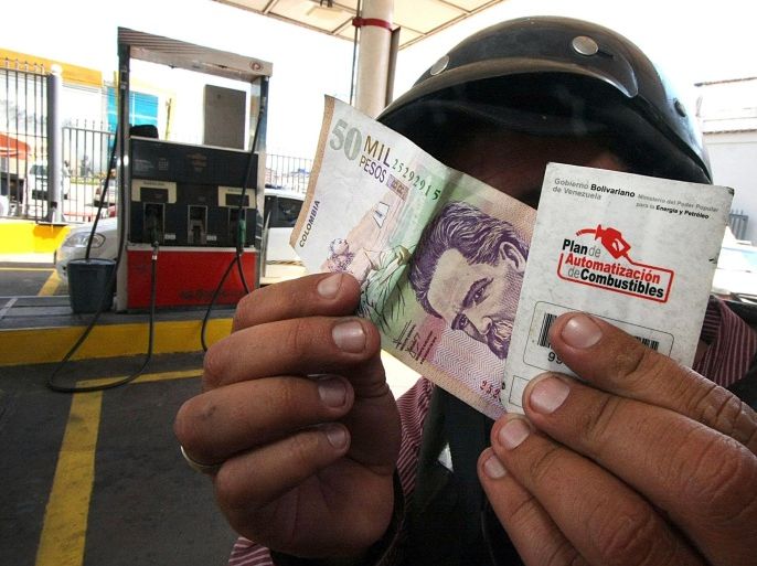 TO GO WITH AFP STORY BY PATRICIA CLAREMBAUXA man shows a card provided by the Venezuelan government to buy fuel and a 50,000 Colombian pesos note at a petrol station in the state of Tachira, Venezuela on May 26, 2014. The lower prices of petrol and basic products in Venezuela encourages contraband towards neighboring Colombia. AFP PHOTO/GEORGE CASTELLANO
