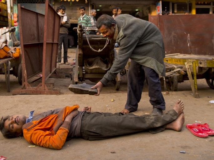 In this Friday, Dec. 12, 2014 photo, a drunk man offers his shoes to his colleague who passed out after consuming alcohol in New Delhi, India. (AP Photo/Saurabh Das)