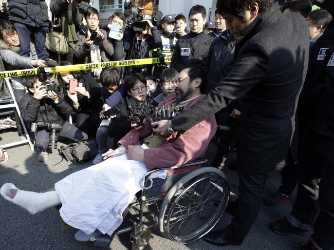 Kim Ki-jong, the suspect of slashing U.S. Ambassador Mark Lippert, in a wheelchair is surrounded by journalists as he leaves a police station for Seoul Central District Court in Seoul, South Korea, Friday, March 6, 2015. Police on Friday investigated the motives of the anti-U.S. activist they say slashed Lippert as questions turned to whether security was neglected. Thursday's attack, which prompted rival North Korea to gloat about "knife slashes of justice," left deep gashes and damaged tendons and nerves. (AP Photo/Lee Jin-man)