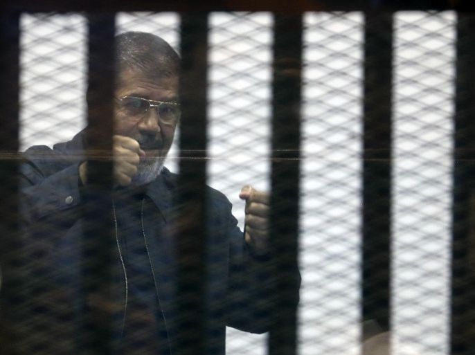 Ousted Islamist President Mohammed Morsi gestures to his defense lawyers from a soundproof glass cage inside a makeshift courtroom as he and others attend a hearing on charges of espionage and leaking classified documents to Qatar, in the Police Academy courthouse in Cairo, Egypt, Tuesday, April, 28, 2015. (AP Photo/Roger Anis, El Shorouk) EGYPT OUT