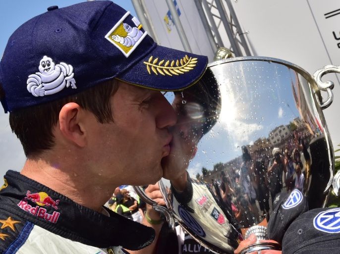 French driver Sebastien Ogier kisses the trophy as he celebrates the first place after winning the 2015 FIA World Rally Championship in Sardegna on June 14, 2015. France's Sebastian Ogier, in a Volkswagen Polo, won the Rally of Sardinia on Sunday finishing ahead of New Zealand's Hayden Paddon and Thierry Neuville of Belgium. Ogier, the two-time world champion, claimed the 28th victory of his career and fourth this season to reinforce his lead at the top of the world rally championship standings. AFP PHOTO / GIUSEPPE CACACE