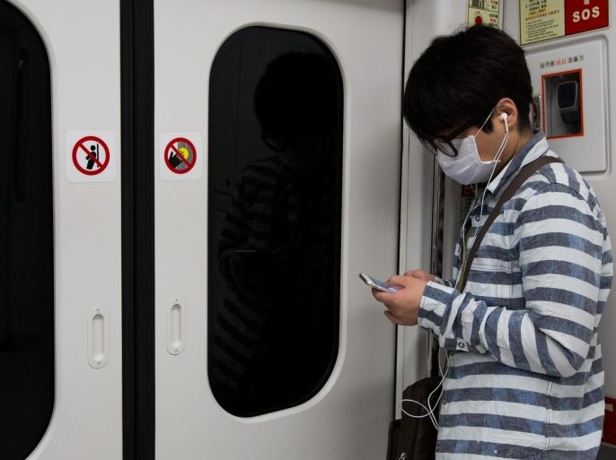 A man wearing a face mask uses a smartphone while riding onboard a subway train in Seoul, South Korea, on Monday, June 8, 2015. South Korea reported its sixth death from the Middle East respiratory syndrome (MERS), with the total number of cases rising to 87, including the first teenager to be infected with the virus.