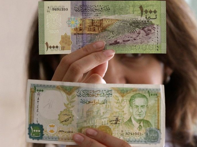 A bank official holds up a new Syrian 1000 pound bank note (background) and the older version bearing the portrait of late Syrian president Hafez al-Assad (foreground), father of current President Bashar al-Assad, on June 30, 2015, following its release by the Central Bank of Syria in Damascus to reinforce the local currency and resist counterfeiting. AFP PHOTO/ LOUAI BESHARA
