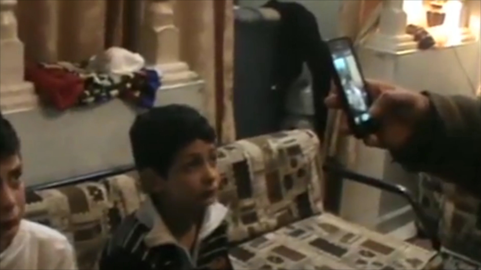 جندي مقنّع يصور طفلا فلسطينيا بعد مداهمة منزله فجرا بمدينة الخليل (الجزيرة)