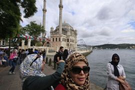 Tourists take pictures at the Ortakoy square in Istanbul, Turkey, backdropped by the Ottoman-era Mecidiye mosque and the Bosporus Bridge, Sunday, June 7, 2015. Turkey is heading to the polls on Sunday in a crucial parliamentary election that will determine whether ruling party lawmakers can rewrite the constitution to bolster the powers of Erdogan. (AP Photo/Lefteris Pitarakis)