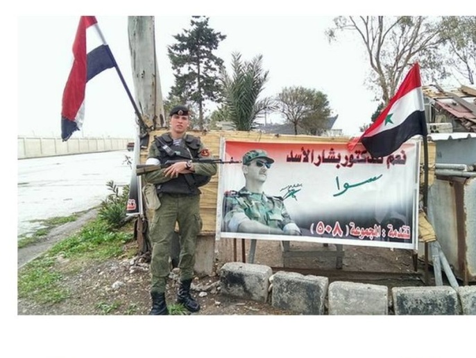 جندي روسي يقف أمام لوحة تحمل صورة بشار الأسد بطرطوس (ناشطون)