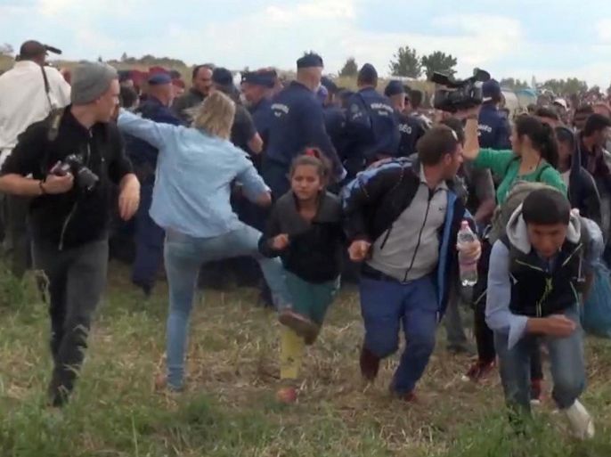 In this image taken from TV a Hungarian camerawoman, center left in blue, kicks out at a young migrant who had just crossed the border from Serbia near Roszke Hungary Tuesday Sept. 8, 2015. The camerawoman has been fired after she was caught on video kicking and tripping migrants entering Hungary across the border with Serbia. The N1TV Internet channel said their employee, widely identified in Hungarian media as Petra Laszlo, has been dismissed because she "behaved unacceptably" at a makeshift gathering point where police take migrants immediately after they enter Hungary near the village of Roszke.(Index.Hu. via AP) HUNGARY OUT