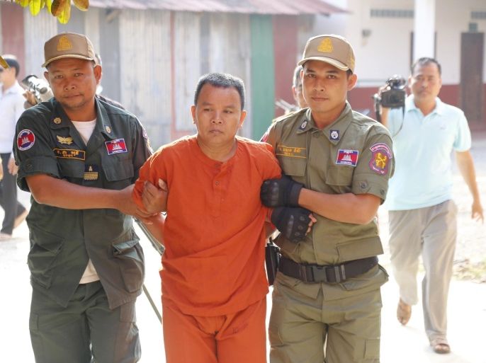 Yem Chhrin, center, an unlicensed medical practitioner, is escorted by prison guards at Battambang provencial court, in Battambang province, northwester of Phnom Penh, Cambodia, Tuesday, Oct. 20, 2015. The medical practitioner who infected more than 100 villagers in northwestern Cambodia with HIV by reusing unclean needles went on trial Tuesday, facing three charges including murder, his lawyer said. (AP Photo)
