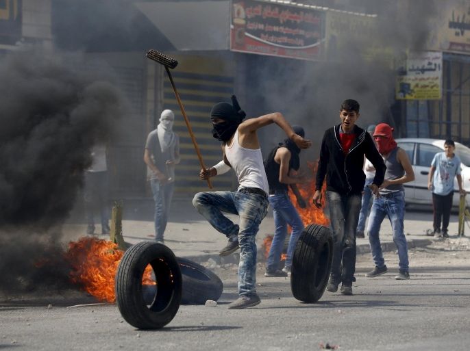 A Palestinian protester moves a burning tyre during clashes with the Israeli army at Qalandia checkpoint near occupied West Bank city of Ramallah October 6, 2015. Palestinian President Mahmoud Abbas said on Tuesday he did not want a spike in deadly violence in East Jerusalem and the Israeli-occupied West Bank to spiral into armed confrontation with Israel. REUTERS/Mohamad Torokman