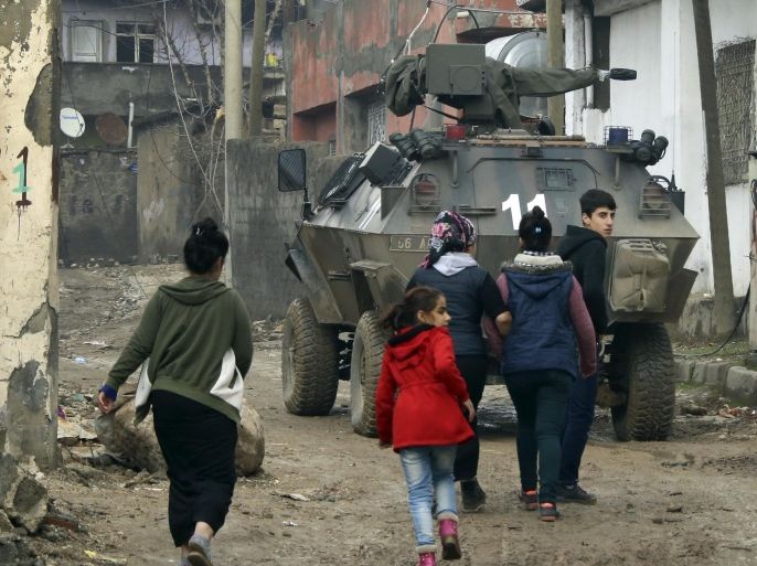Backdropped by a Turkish forces armoured personnel carrier, residents walk around after the 24-hour curfew was lifted, in the mostly-Kurdish town of Silopi, in southeastern Turkey, near the border with Iraq, Tuesday, Jan. 19, 2016. Turkey's prime minister announced Tuesday that military operations against Kurdish rebels have ended in one mainly Kurdish southeastern town. The military is still fighting militants linked to the Kurdistan Workers' Party, or PKK, in two other urban areas. (AP Photo/Mahmut Bozarslan)