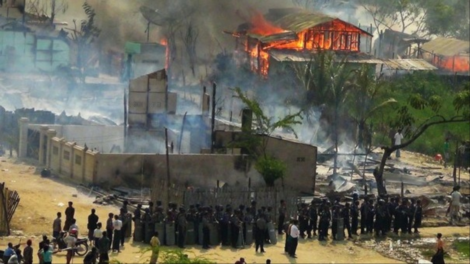 ‪صورة تعود لعام 2012 تظهر إحراق البوذيين منازل الروهينغا بينما يصطف العسكر الميانماري متفرجا‬ (الجزيرة)