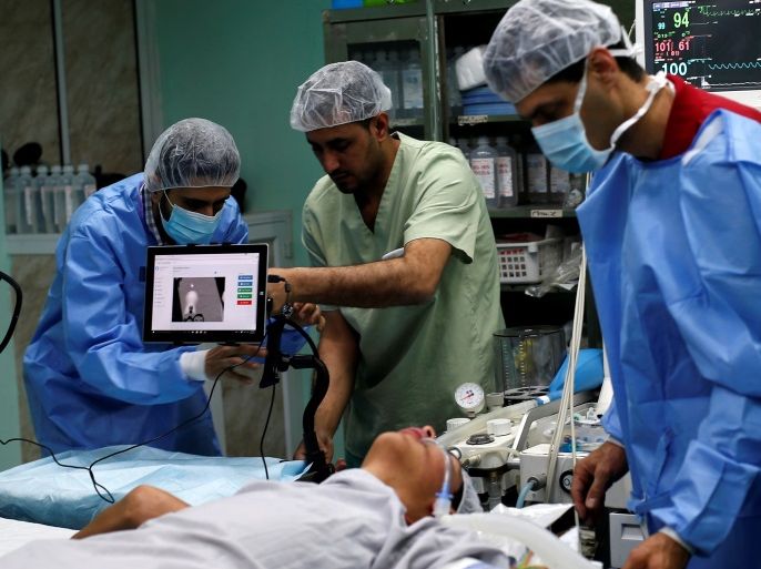 A patient lies on a bed as a technician (L) adjusts a screen before the start of a Proximie surgery, with doctor Ghassan Abu Sitta in Beirut guiding Palestinian surgeon Hafez Abu Khousa in the operating room at Al Awda Hospital in the northern Gaza Strip April 30, 2016. REUTERS/Suhaib Salem