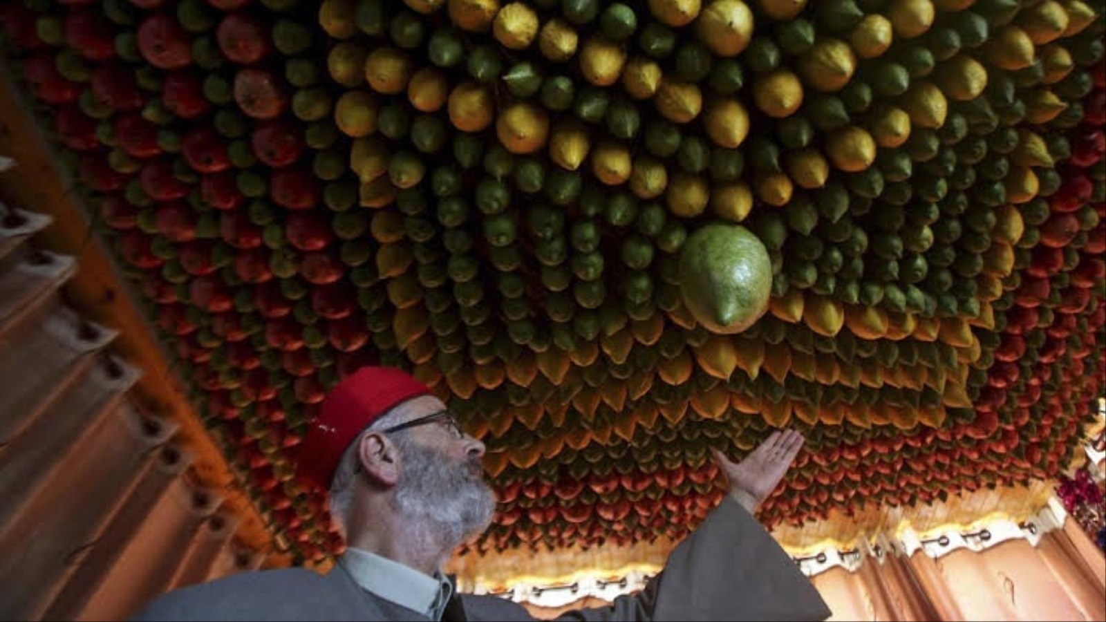 الكاهن حسني ينظر إلى سقف منزله المزين بأنواع الفواكه المختلفة خلال عيد العرش (الجزيرة)